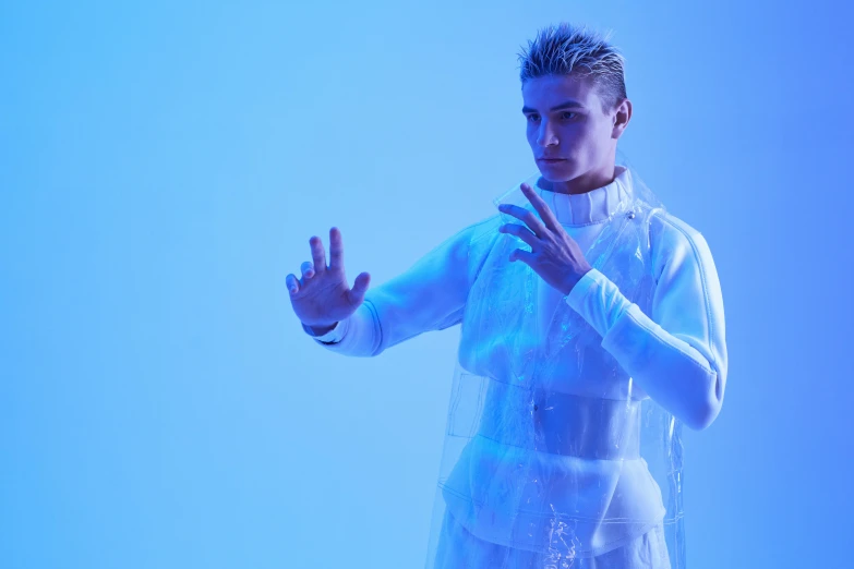 a man standing in front of a blue background, an album cover, inspired by Kristian Kreković, holography, white clothing, model is wearing techtical vest, covered in transparent cloth, behind the scenes photo