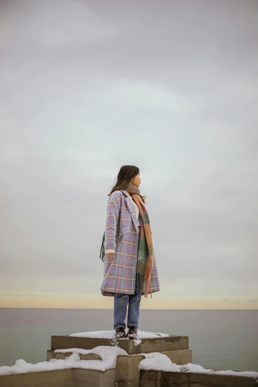 a woman standing on top of a snow covered pier, unsplash, conceptual art, tartan cloak, multi colored, long coat, overlooking the beach