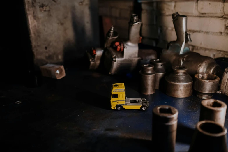 a yellow toy truck sitting on top of a table, by Daniel Lieske, pexels contest winner, arbeitsrat für kunst, working in the forge, tiny details, metal towers and sewers, low-key light