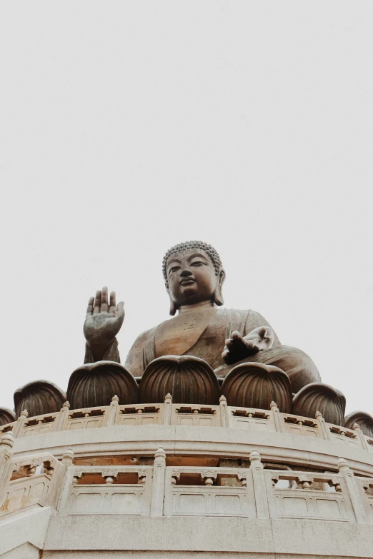 a large statue of buddha sitting on top of a building, by Patrick Ching, trending on unsplash, wave a hand at the camera, low quality photo, hong kong, brown