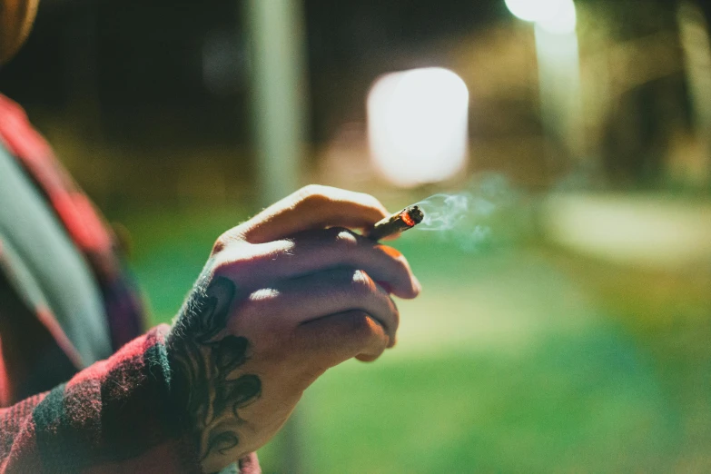 a close up of a person holding a cigarette, a tattoo, pexels contest winner, a green, sunfaded, bright flare, beautiful surroundings