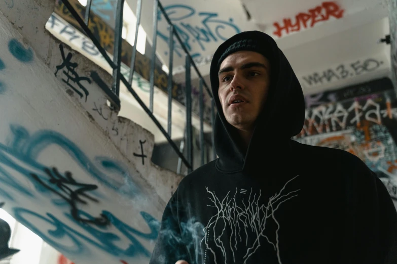 a man in a black hoodie holding a skateboard, pexels contest winner, graffiti, covered in runes, looking serious, profile picture 1024px, with prison clothing