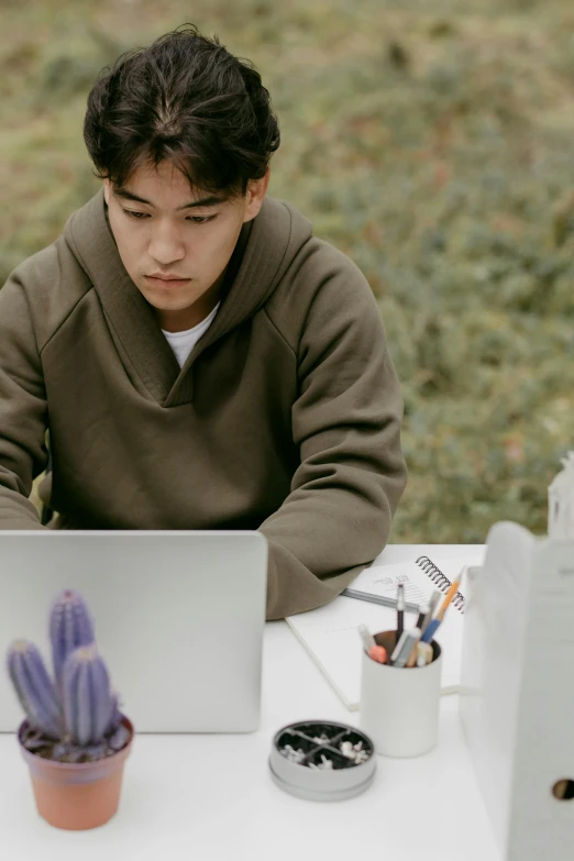 a man sitting at a table with a laptop computer, damien tran, trying to study, at a clearing, looking serious