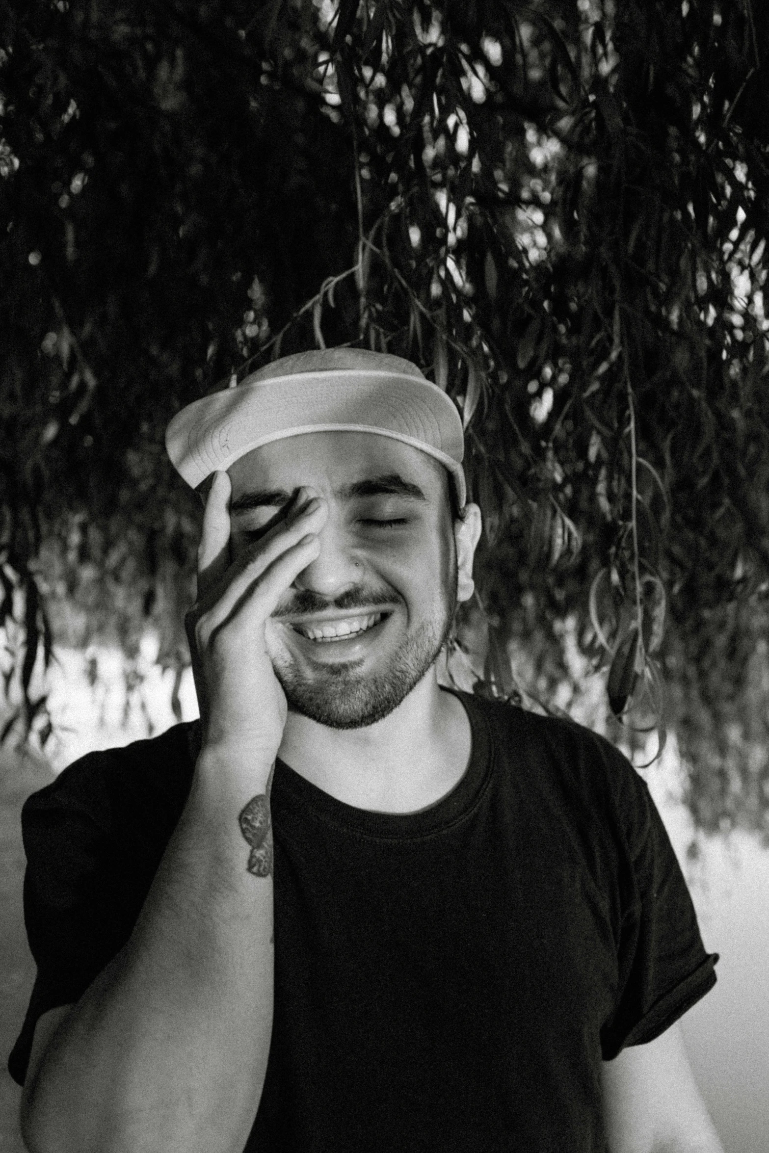 a man talking on a cell phone under a tree, a black and white photo, inspired by Alexis Grimou, pexels contest winner, realism, goofy smile, mac miller, wears a destroyed hat, discord profile picture