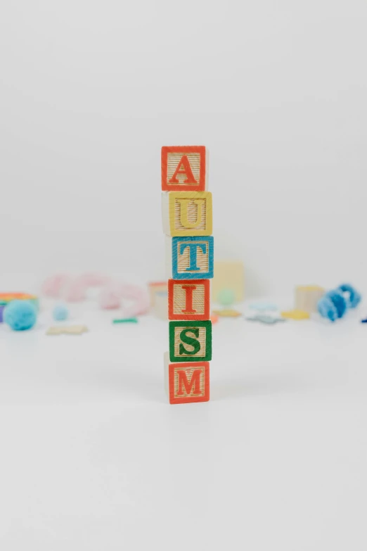 a stack of wooden blocks spelling autism, by Ruth Simpson, letterism, full body photograph, multicoloured