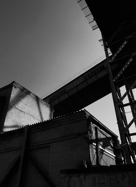 a black and white photo of a building under a bridge, by Tobias Stimmer, unsplash, brutalism, factories, back alley, silhouette :7, sunny day