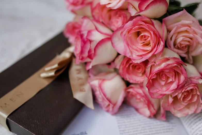 a bunch of pink roses sitting on top of a book, by Alice Mason, unsplash, ribbon, close up details, reading the book about love, brown and pink color scheme