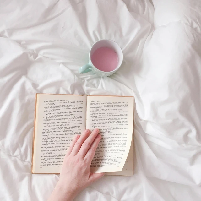 a person reading a book on a bed with a cup of tea, by Carey Morris, pexels, white and pink cloth, battered, instagram post, plain background