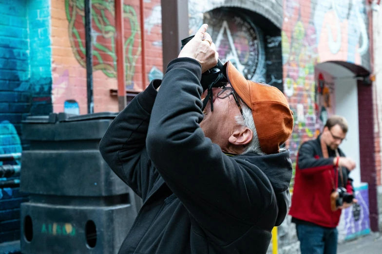 a man taking a picture of graffiti on the side of a building, a photo, binoculars, hood covers his eyes, behind the scenes photography, chinatown