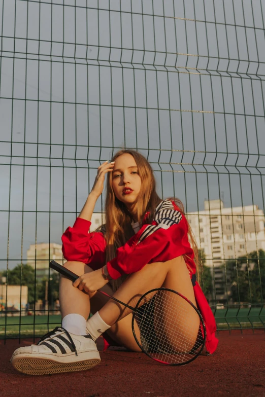 a woman sitting on the ground with a tennis racket, inspired by Elsa Bleda, trending on pexels, realism, cool red jacket, on a soccer field, portrait sophie mudd, red mesh in the facede