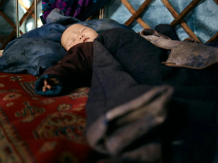 a baby laying on top of a bed covered in blankets, by Elsa Bleda, pexels contest winner, hurufiyya, mongolia, shamanistic dark blue clothes, tribal yurta, highly detaild