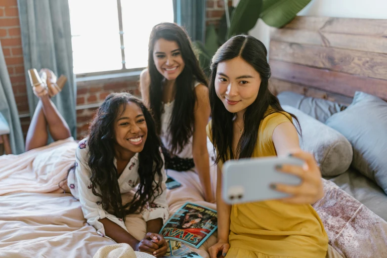 a group of young women sitting on top of a bed, a picture, trending on pexels, iphone selfie, three women, asian descent, on a yellow canva