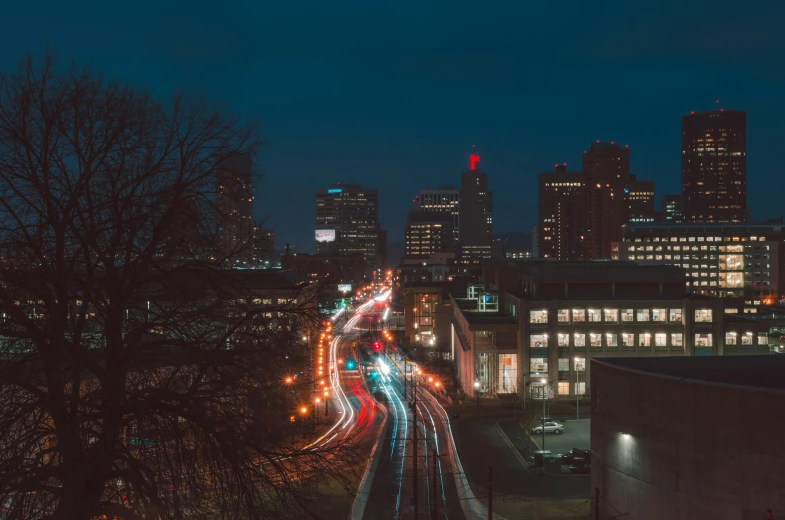 a street filled with lots of traffic next to tall buildings, by Carey Morris, unsplash contest winner, visual art, distant town lights, rhode island, city buildings on top of trees, coventry city centre