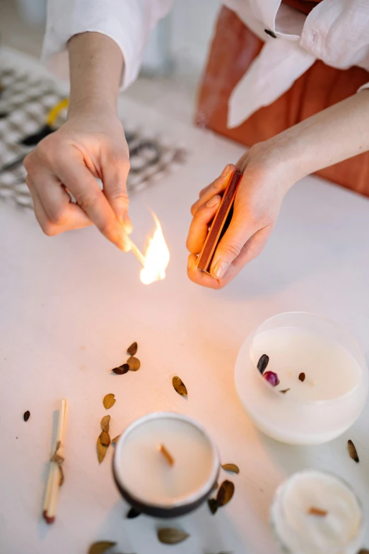 a person lighting a candle on a table, a still life, by Julia Pishtar, process art, s'mores, with glow on some of its parts, seeds, product design shot