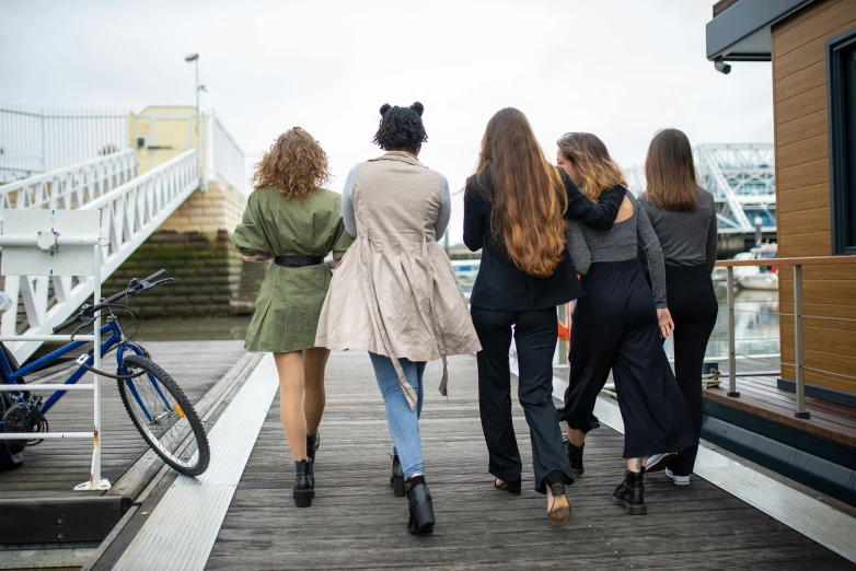 a group of women walking down a wooden walkway, trending on pexels, long hairs, wearing jacket and skirt, femalev beauty, lesbians