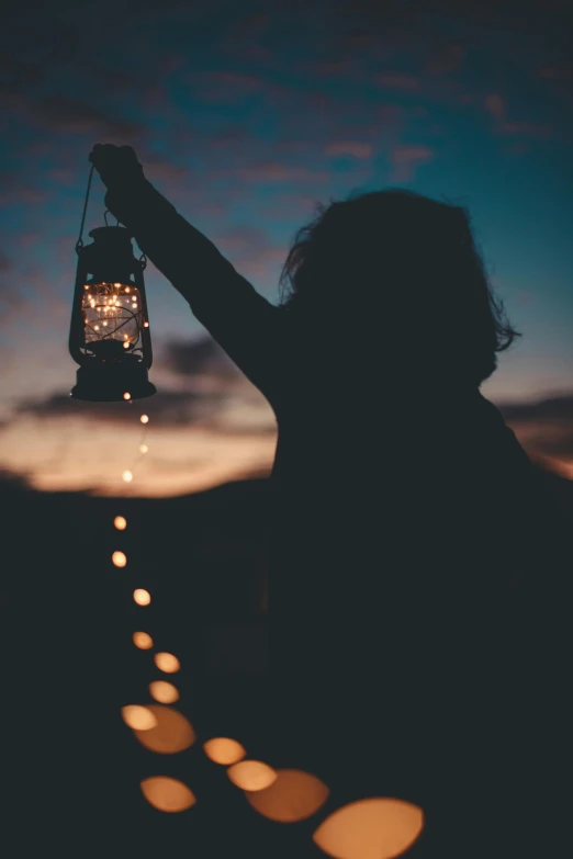 a person holding a lantern in the dark, pexels contest winner, minimalism, fairy lights, silhouette over sunset, muted lights, well lit sky
