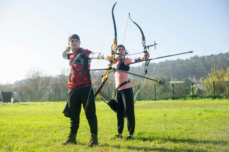 a couple of people standing on top of a lush green field, archery, avatar image, sports photo, icaro carvalho