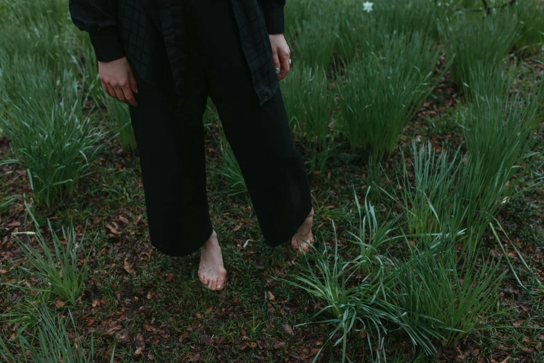 a woman standing in a field of tall grass, unsplash, black sweatpants, wearing black silk robe, exposed toes, next to a plant