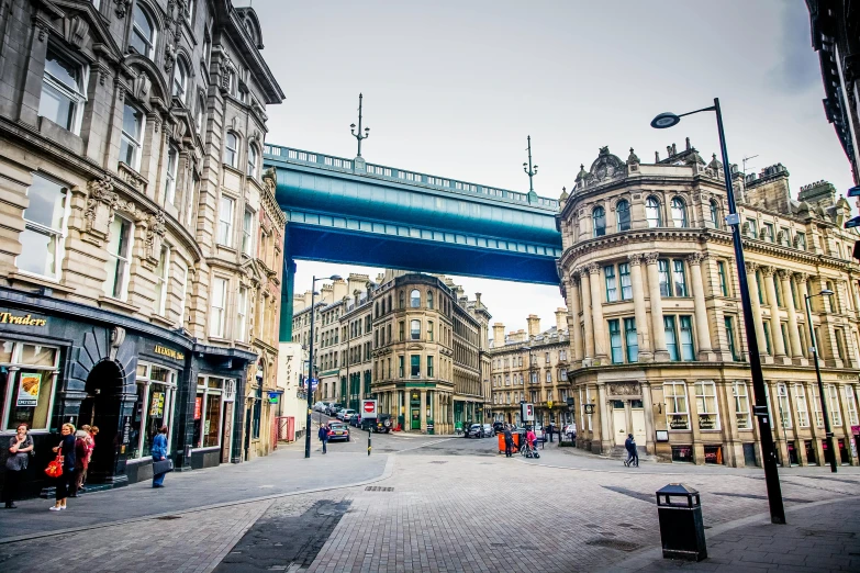 a group of people walking down a street next to tall buildings, inspired by Gawen Hamilton, art nouveau, sitting under bridge, yorkshire, victorian arcs of sand, beautiful city