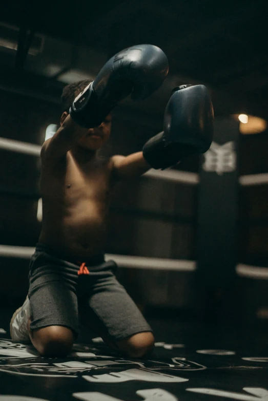 a man sitting on the ground in a boxing ring, pexels contest winner, black boy shorts, holding it out to the camera, worksafe. cinematic, little kid