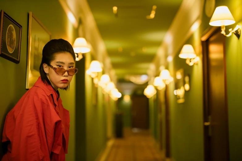 a woman leaning against a wall in a hallway, inspired by Elsa Bleda, pexels contest winner, wearing red and yellow clothes, wong kar wai, hotel room, wearing gold glasses