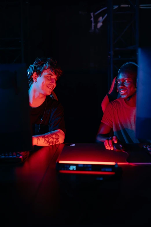 two people sitting at a table in front of a computer, pexels, computer art, red and blue black light, gaming room, college party, two young men