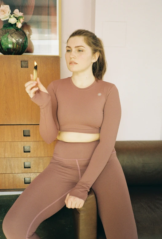 a woman sitting on a stool holding a cigarette, featured on instagram, two piece workout clothes, sitting on a mocha-colored table, 🎀 🧟 🍓 🧚, wearing a track suit