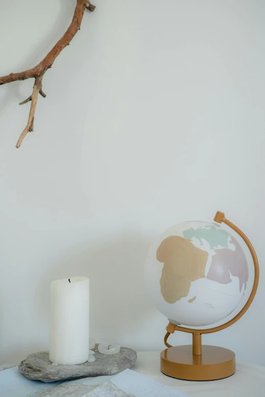 a globe sitting on top of a table next to a candle, nordic pastel colors, dwell, close body shot, muted colors. ue 5
