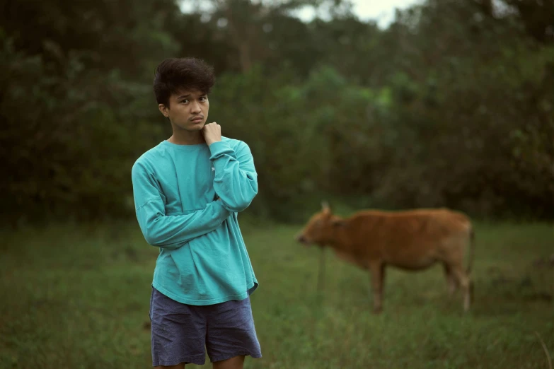a young boy standing in a field next to a cow, an album cover, pexels contest winner, sumatraism, with teal clothes, movie still 8 k, set on singaporean aesthetic, young man