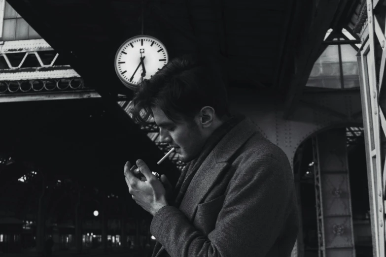 a black and white photo of a man smoking a cigarette, inspired by Vivian Maier, pexels contest winner, surrealism, clock, train station, looking at his phone, extremely handsome