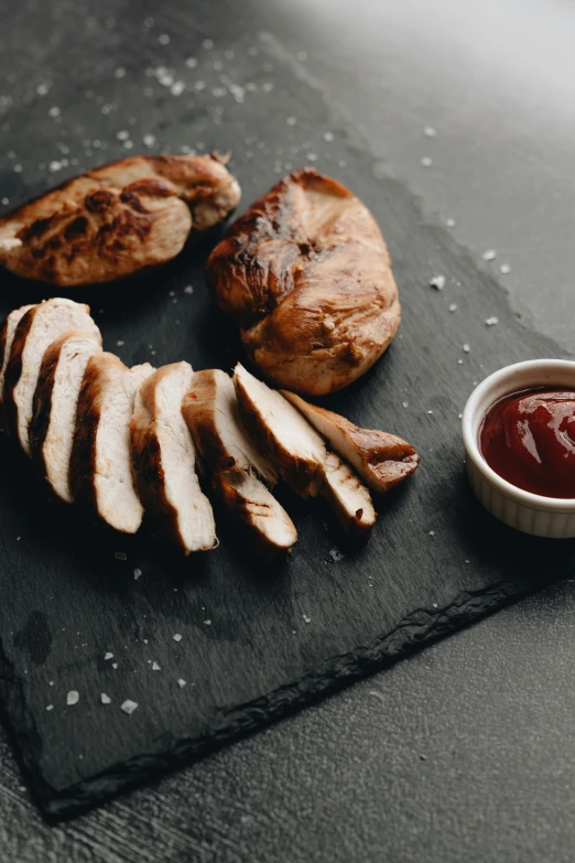 a cutting board topped with sliced chicken next to a bowl of ketchup, pexels contest winner, renaissance, dark backdrop, manuka, 6 pack, grilled chicken