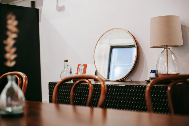 a dining room table with chairs and a mirror on the wall, pexels contest winner, light and space, circle face, doctors mirror, black and terracotta, wood table