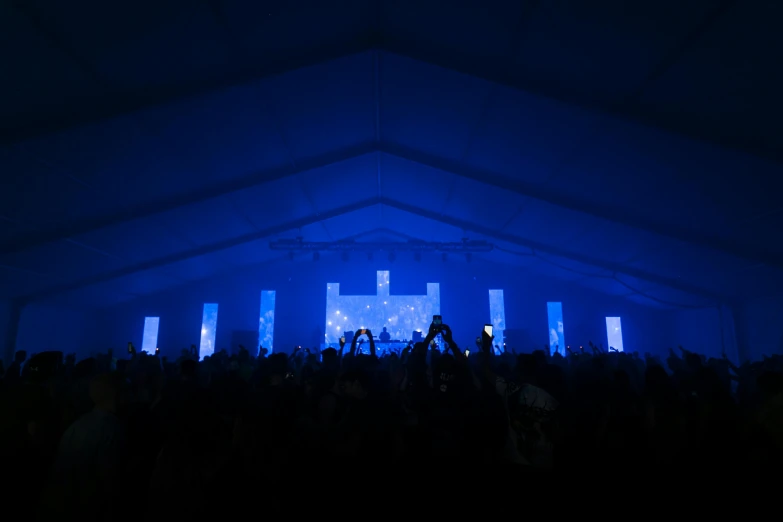 a large group of people standing in front of a stage, by Sebastian Vrancx, light and space, mellow sky blue lighting, interior of a tent, 5000k white product lighting, vaporwave lighting
