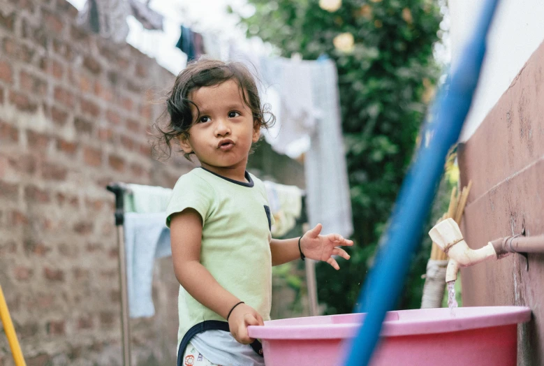 a little girl standing next to a pink tub, pexels contest winner, dirty clothes, peruvian boy looking, indian girl with brown skin, 2 years old