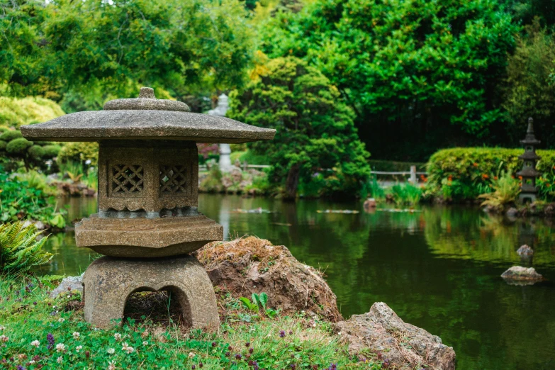 a stone lantern sitting on top of a lush green field, inspired by Tōshi Yoshida, unsplash, sōsaku hanga, garden pond scene, parks and public space, 90s photo