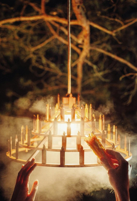 a person holding a candle in front of a chandelier, by Romain brook, land art, teepee, promo image, carousel, forest ray light
