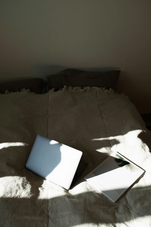 a laptop computer sitting on top of a bed, by Elsa Bleda, unsplash, light and space, big shadows, rinko kawauchi, beds, sun dappled