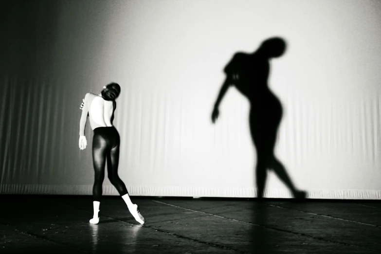 a woman standing in front of a shadow of a man, a black and white photo, arabesque, wearing white leotard, jemal shabazz, foreground, instagram photo