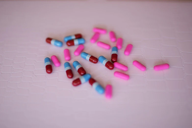 a pile of pills sitting on top of a table, by Rachel Reckitt, unsplash, plasticien, magenta and crimson and cyan, on a white table, lined up horizontally, alien capsules