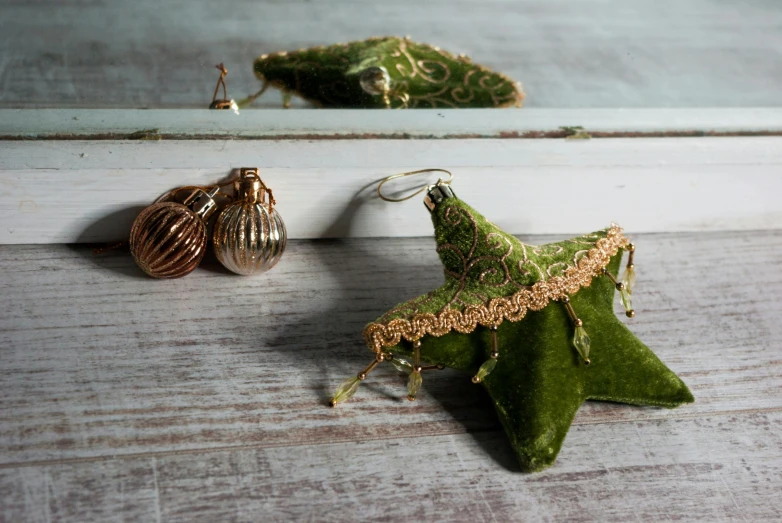 a close up of a star ornament on a table, a still life, by Sylvia Wishart, pexels, arabesque, wearing elaborate green and gold, with small studded earings, embroidered velvet, miniature product photo