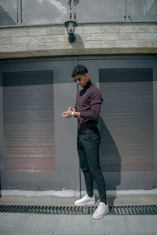 a man standing on a sidewalk looking at his cell phone, an album cover, by Robbie Trevino, pexels contest winner, purple and black clothes, brown pants, mohamed chahin, doing an elegant pose