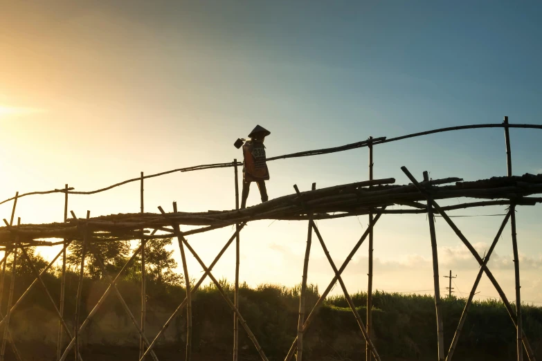 a person standing on top of a wooden bridge, happening, thatched roof, sun setting, scaffolding, farming