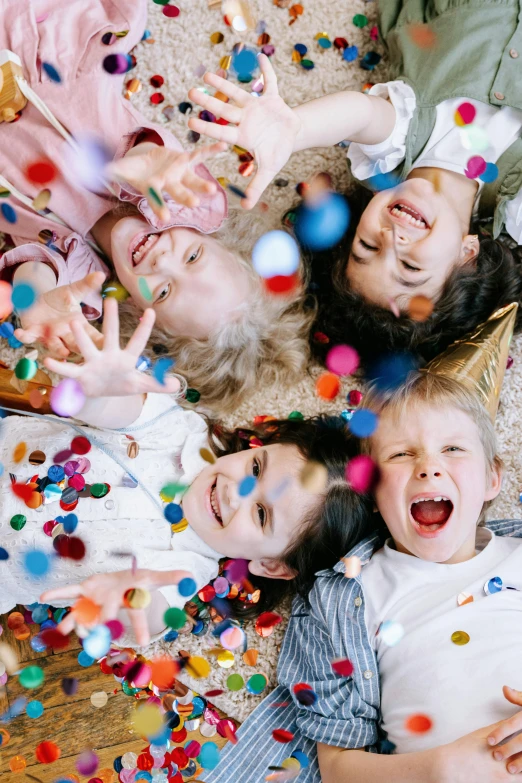 a group of children laying on the floor surrounded by confetti, zoomed in, clowns, full product shot, petite