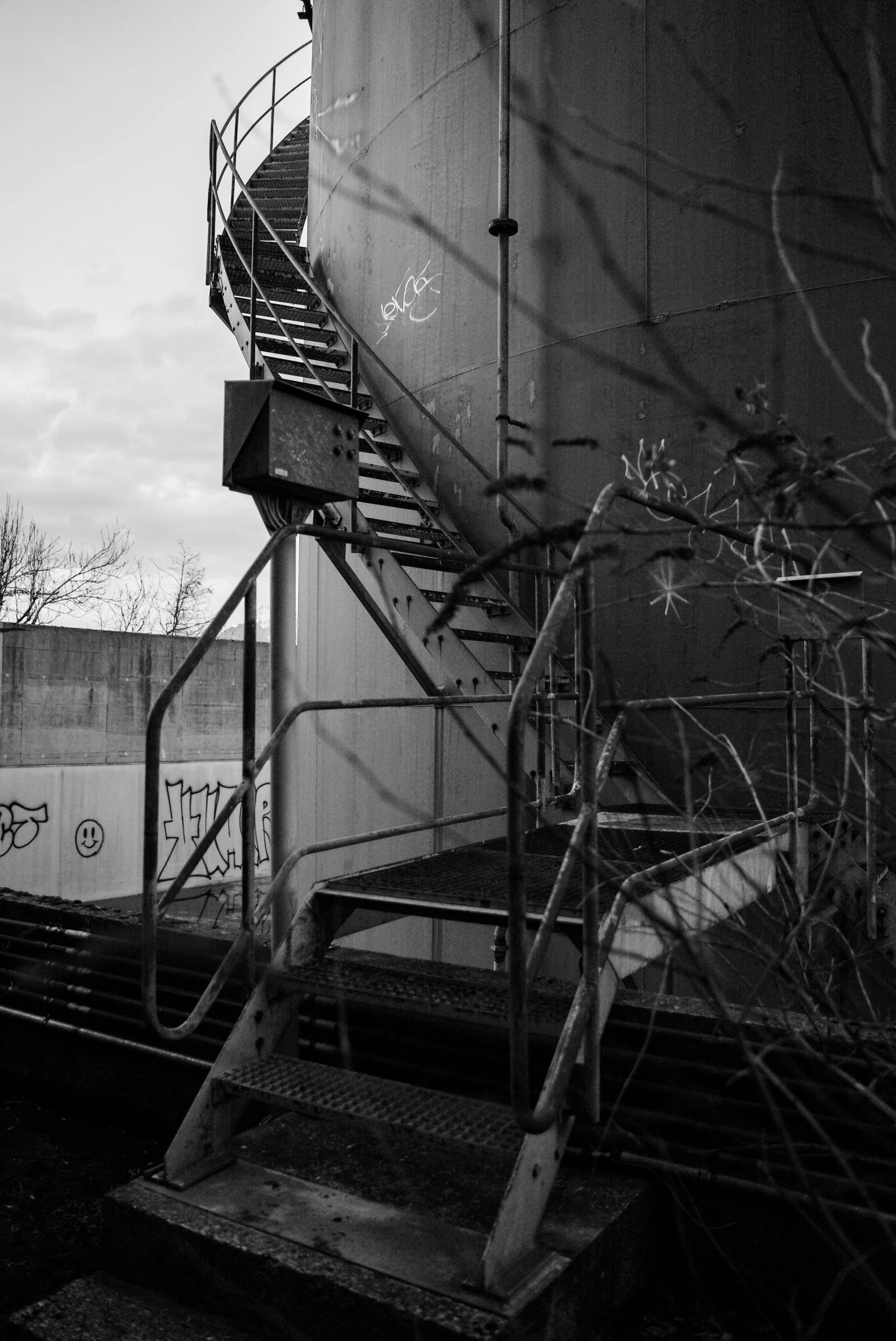 a black and white photo of a train track, a black and white photo, brutalism, outdoor staircase, overgrown spamp, industrial colours, late evening