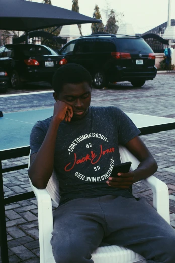 a man sitting on a white chair talking on a cell phone, by Chinwe Chukwuogo-Roy, pexels contest winner, wearing a t-shirt, he is about 20 years old, isaac zuren, slightly smirking