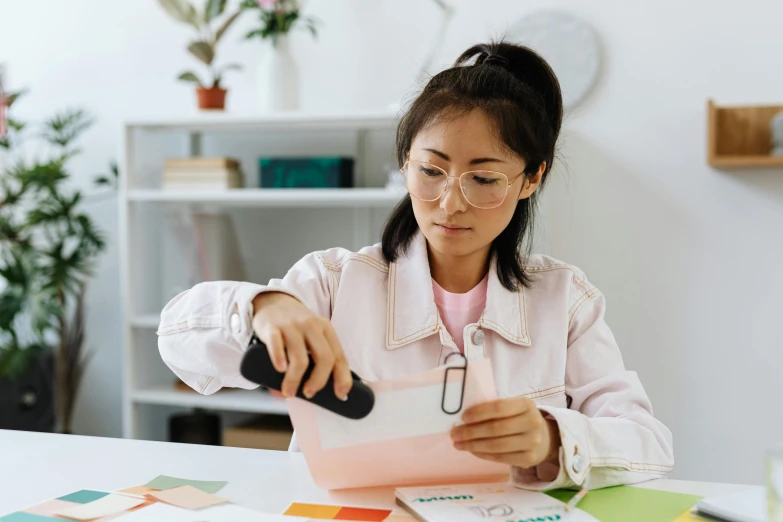 a woman sitting at a table looking at a piece of paper, by Jang Seung-eop, pexels contest winner, holding a clipboard, avatar image, educational supplies, woman with rose tinted glasses