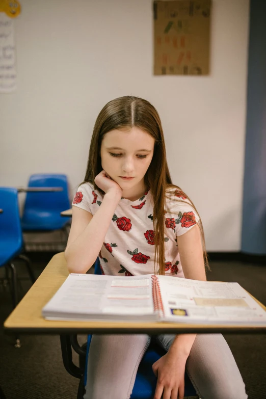 a girl sitting at a desk reading a book, looking serious, taken in 2 0 2 0, in a classroom, high quality photo