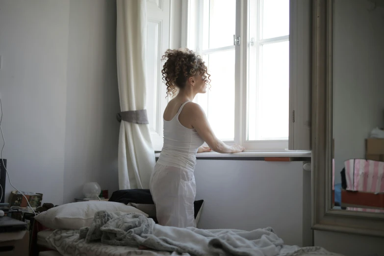 a woman standing in front of a window in a bedroom, pexels contest winner, happening, white and grey, looking left, resting, gif