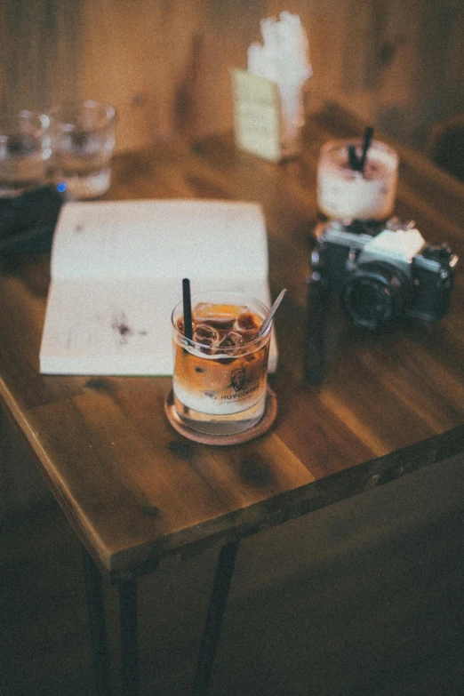 a wooden table topped with a glass filled with liquid, a polaroid photo, trending on unsplash, whiskey, ice coffee, reading for a party, medium format