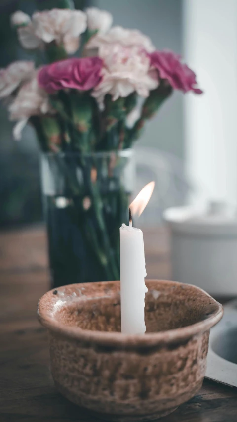 a candle sitting on top of a table next to a vase of flowers, trending on unsplash, paul barson, pestle, natural soft rim light, shot from the side